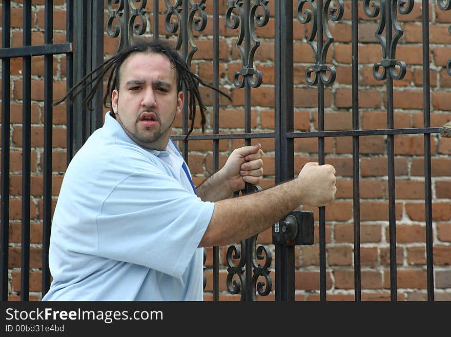 Photo of a young man standing on the sidewalk grasping a gate enterance. Photo of a young man standing on the sidewalk grasping a gate enterance