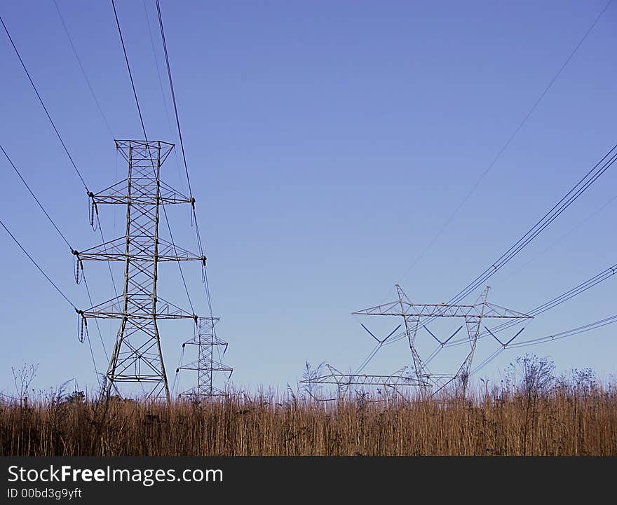 Open grass field with high power electrical pylons and blue sky. Open grass field with high power electrical pylons and blue sky