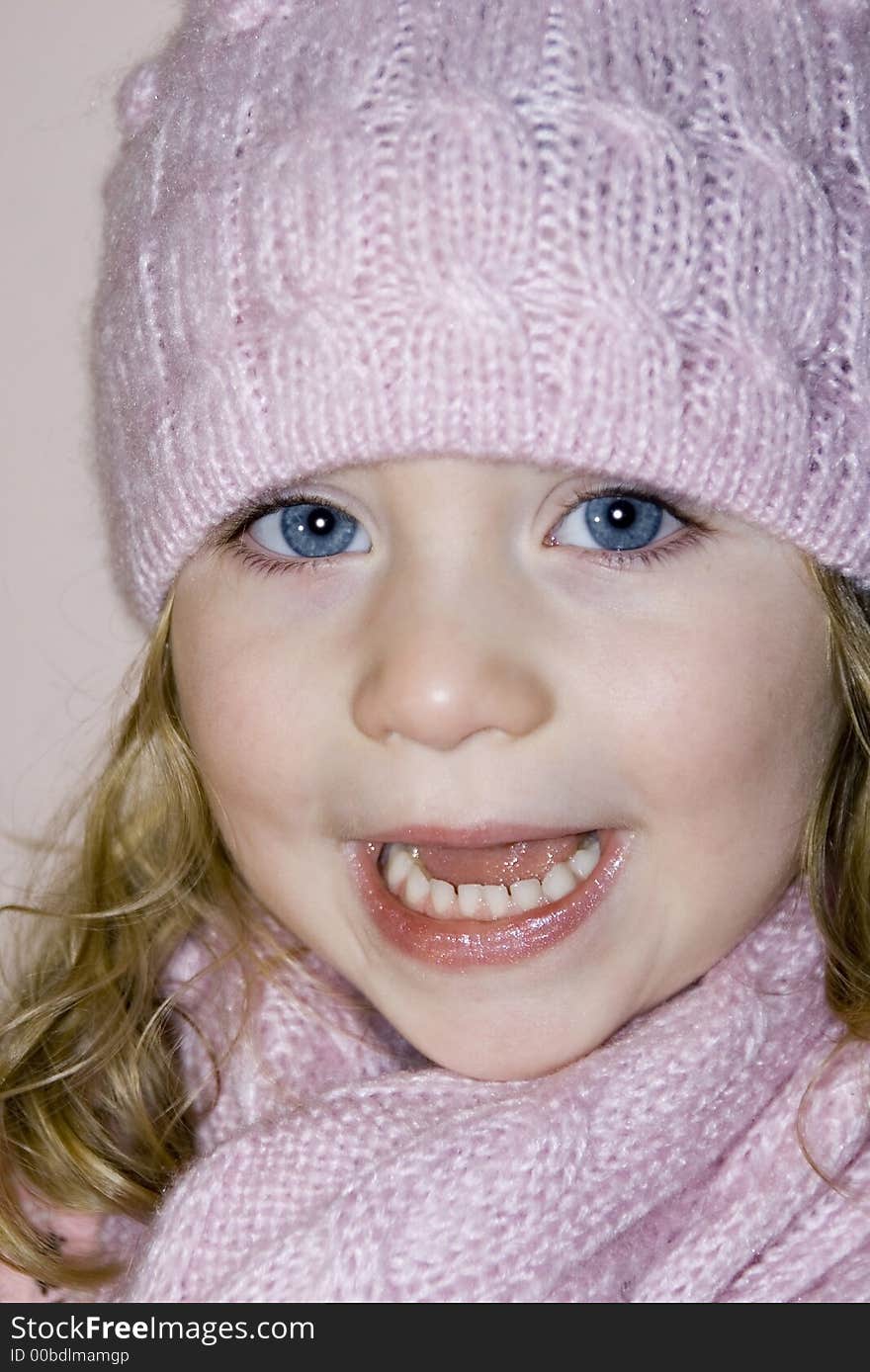 Cute blue eyed girl with matching pink hat and scarf and blond curls laughing in the camera. Cute blue eyed girl with matching pink hat and scarf and blond curls laughing in the camera