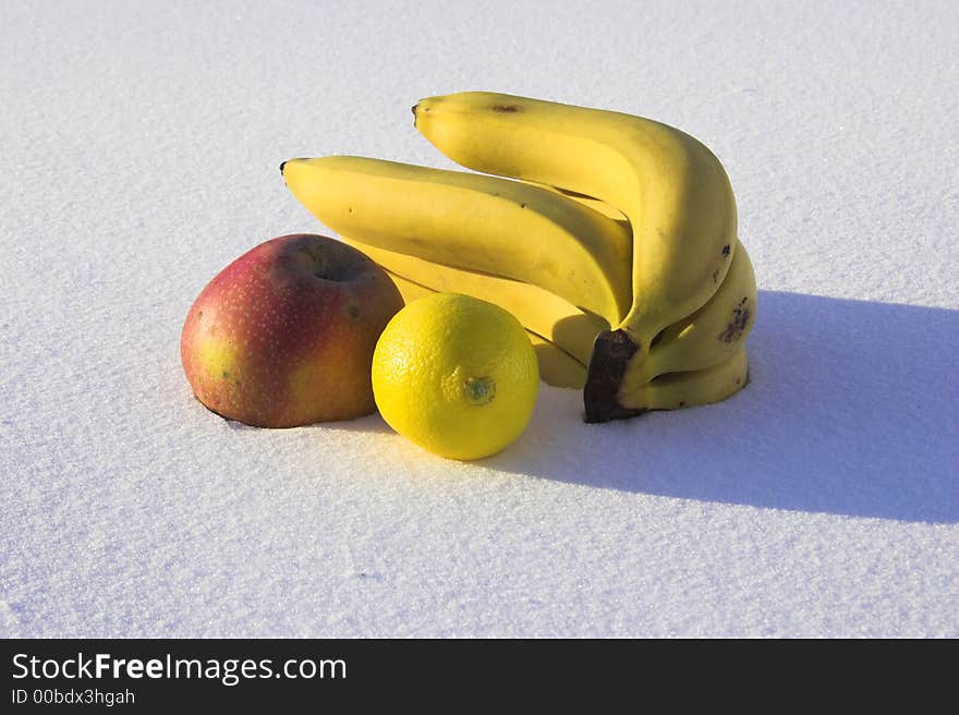 Bananas, mandarin, apple and lemon on the snow with shadow. Bananas, mandarin, apple and lemon on the snow with shadow