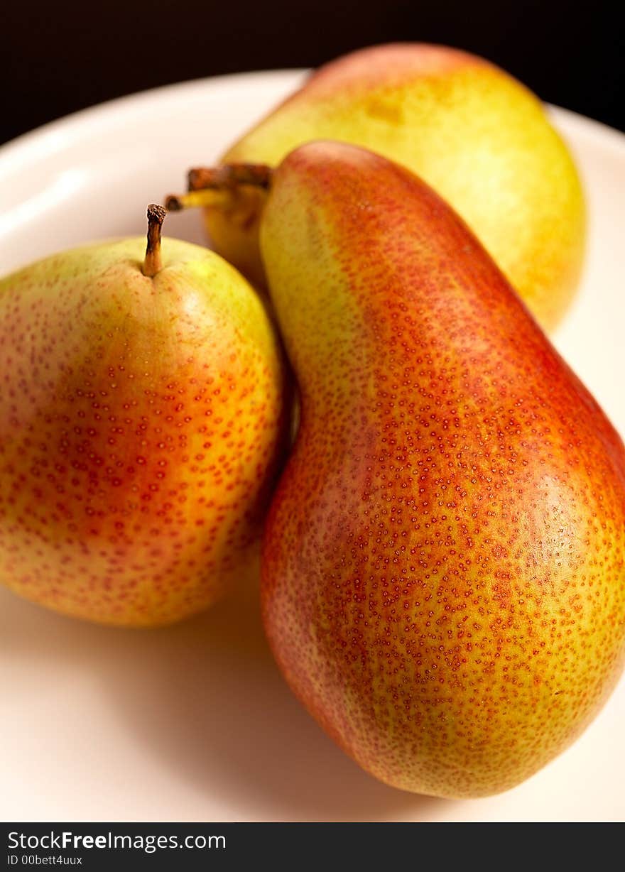 Three pears on white plate on black background