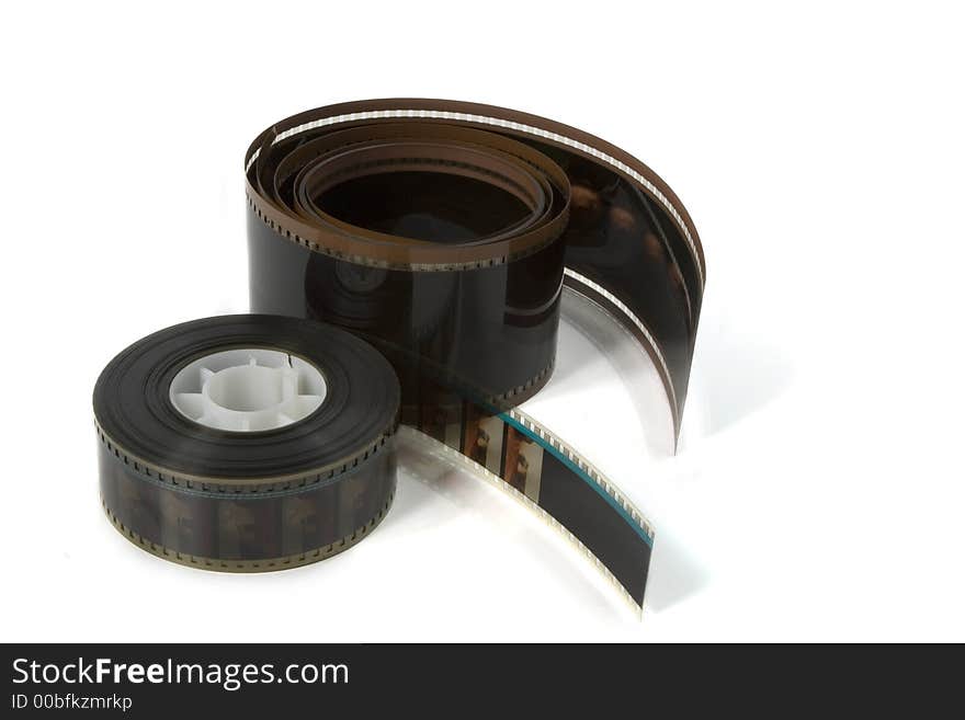 A curled strip of old 70mm movie film next to a reel of 35mm film- on white. A curled strip of old 70mm movie film next to a reel of 35mm film- on white