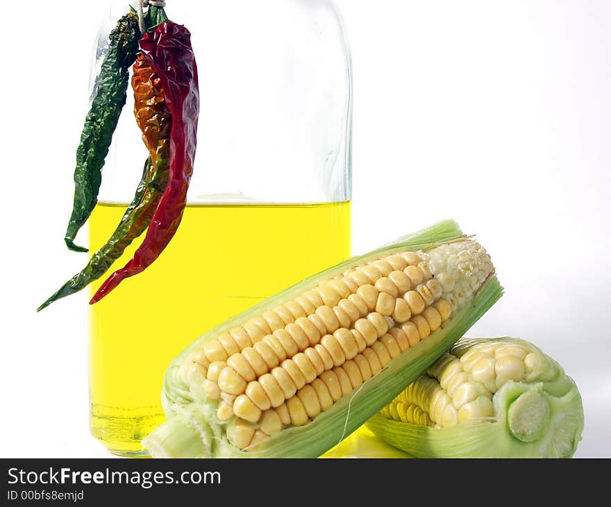 Bottle of yellow oil and fresh corn on the cob with pepper