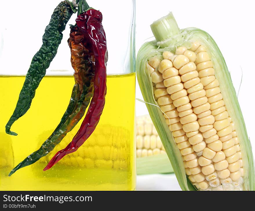 Bottle of yellow oil and fresh corn on the cob with pepper