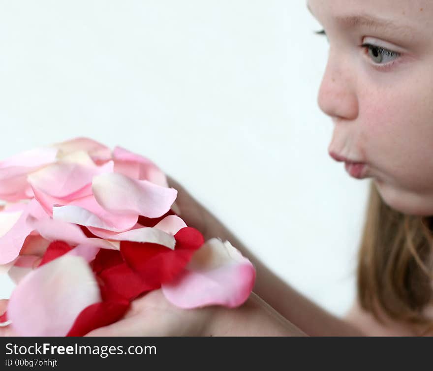 Young girl blowing pink, red, white rose petals held in hands. Young girl blowing pink, red, white rose petals held in hands