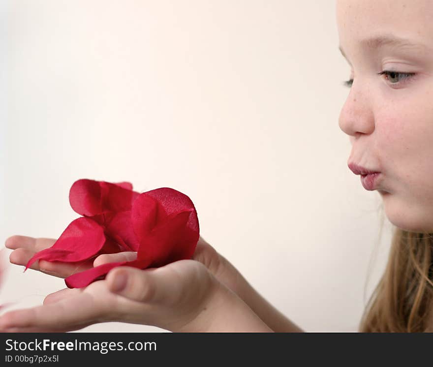 Young girl blowing pink, red, white rose petals held in hands over a slightly pink background. Young girl blowing pink, red, white rose petals held in hands over a slightly pink background