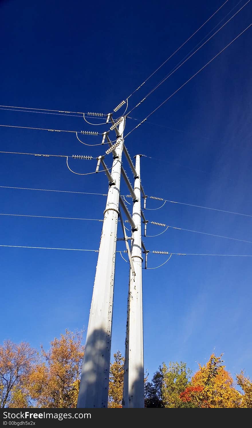 Power lines towers over autumn treetops - blue sky with wispy clouds to right. Power lines towers over autumn treetops - blue sky with wispy clouds to right