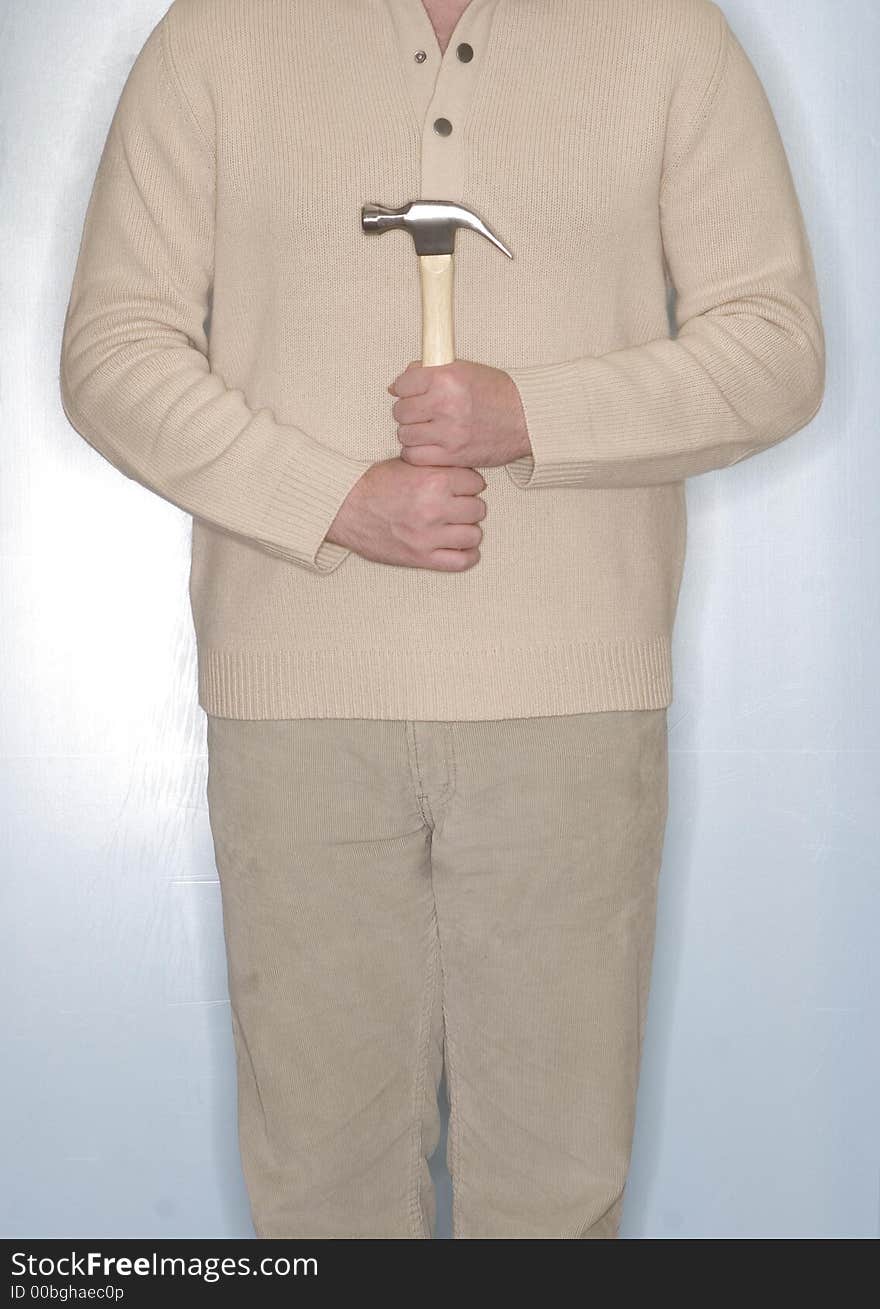 Man dressed in off-white clothing holds a hammer in front of his body while he stands in front of a blue background. Man dressed in off-white clothing holds a hammer in front of his body while he stands in front of a blue background