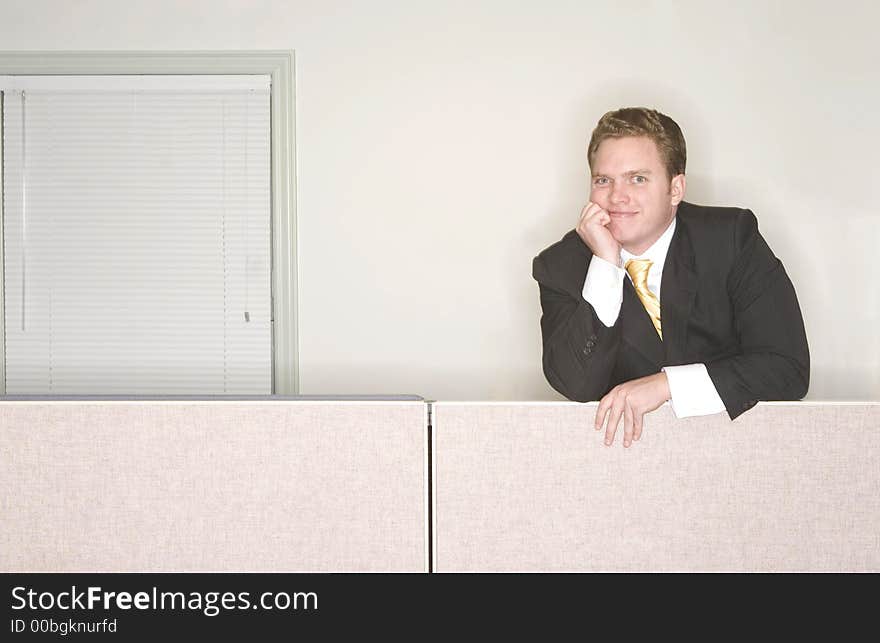 Businessman smiles with his hand on his chin standing above his office cubicle