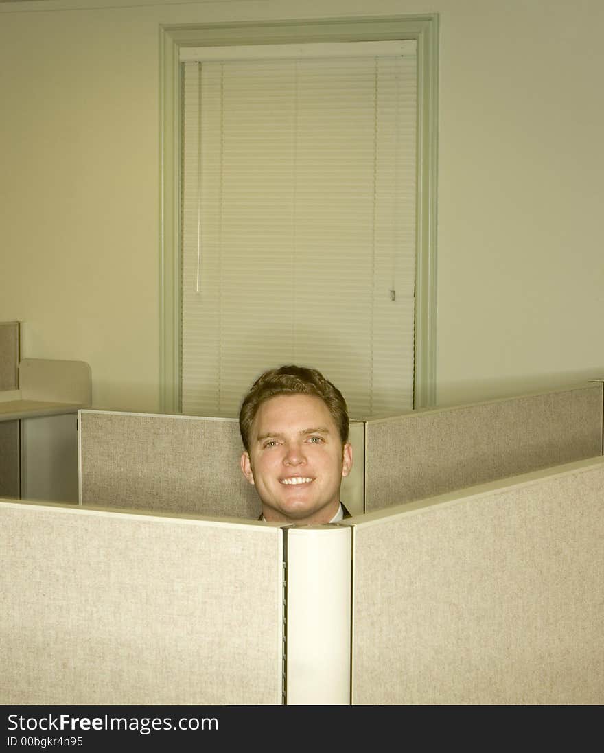 Businessman smiles and shows his head above the office cubicles