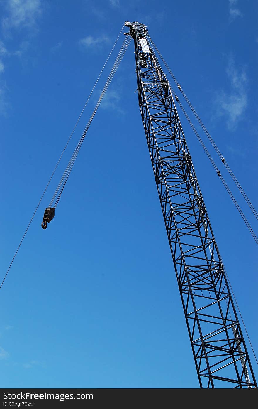 Silhouette of crane and hook against blue sky and some cloud