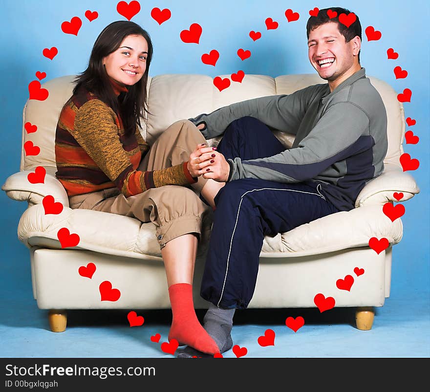 The young couple sitting on a sofa surrounded by rendered hearts