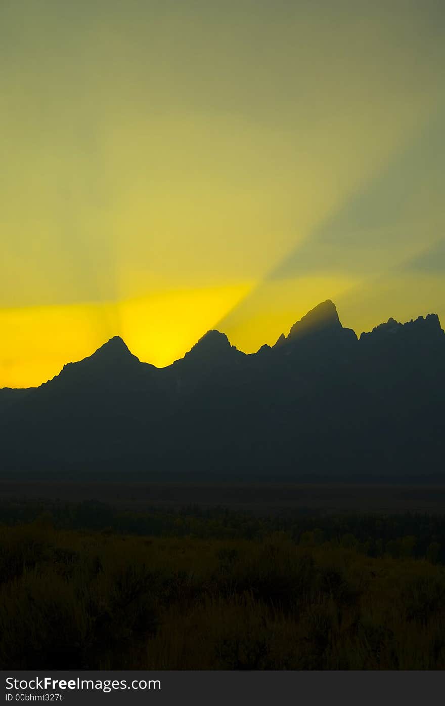 Sunbeams brighten the sky at sunset over the silhouetted mountains in Grand Teton National Park. Sunbeams brighten the sky at sunset over the silhouetted mountains in Grand Teton National Park