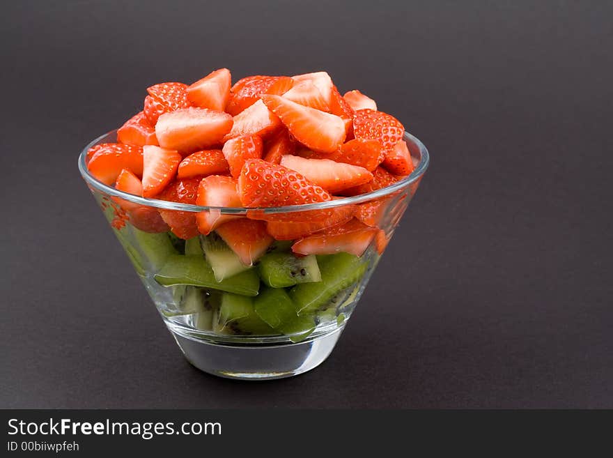 Strawberries with kiwi in transparent bowl on dark background. Healthy suggestion.