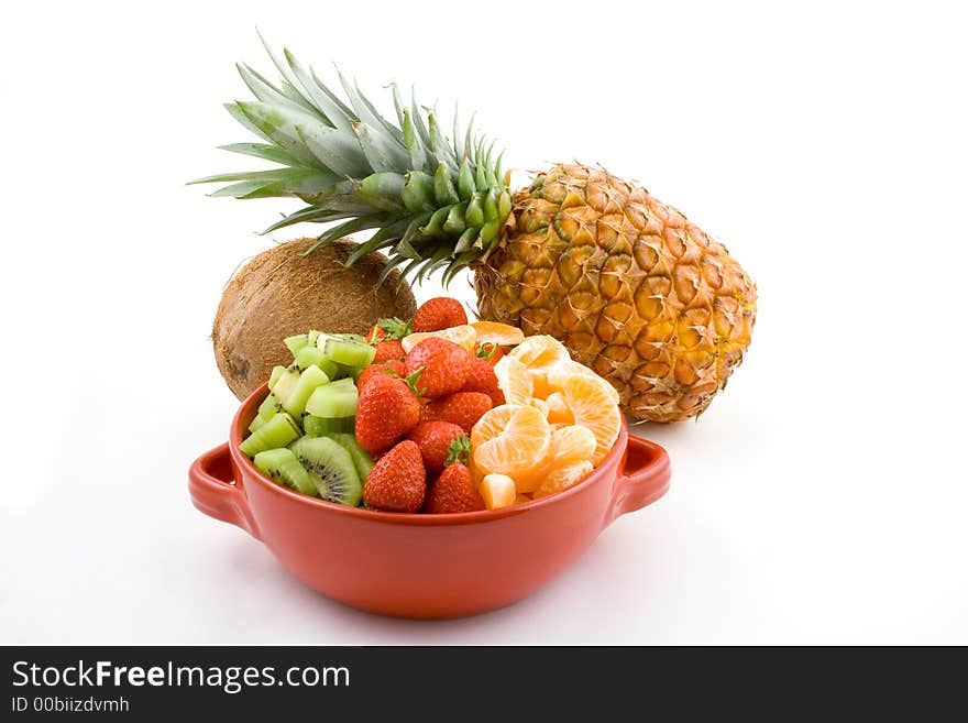 Some fruit mixture, strawberries kiwi and tangerine in red bowl with pineapple and coconut in the background. Some fruit mixture, strawberries kiwi and tangerine in red bowl with pineapple and coconut in the background.