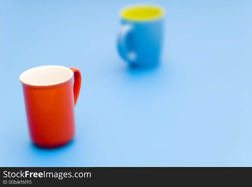 Abstract of red cup with interior white, and blue cup with interior yellow, taken on a light blue background. Red cup in front is in focus; blue cup in back is not. Abstract of red cup with interior white, and blue cup with interior yellow, taken on a light blue background. Red cup in front is in focus; blue cup in back is not.