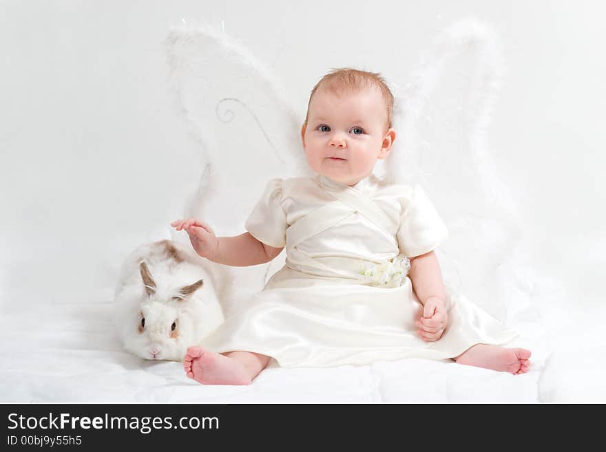 Cute little girl dressed like fairy with fluffy wings plays with white rabbit. Cute little girl dressed like fairy with fluffy wings plays with white rabbit