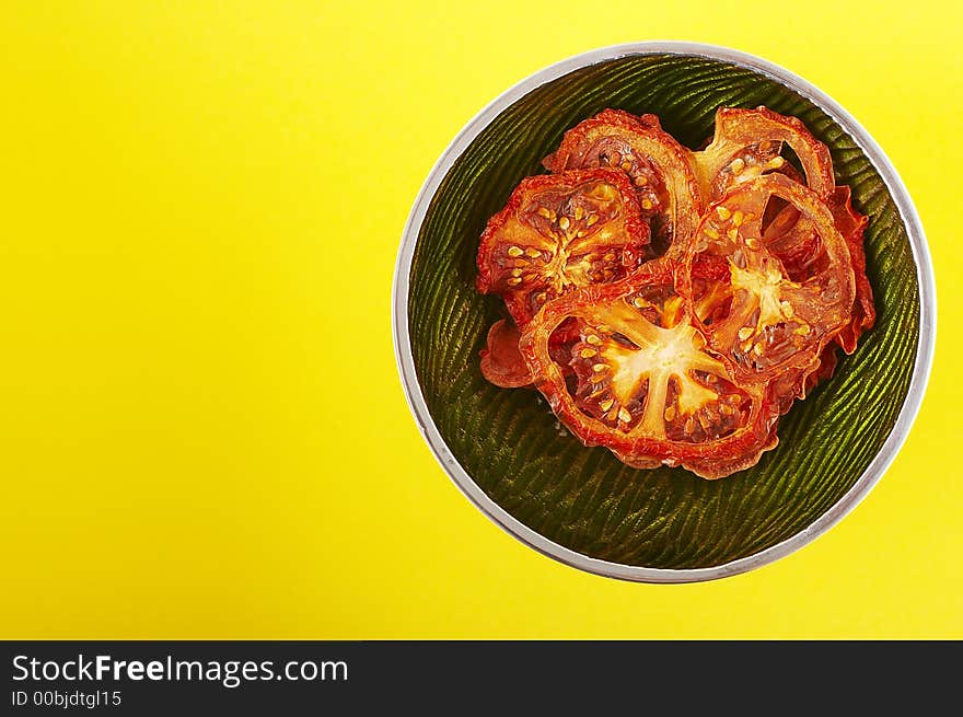 Dried sliced tomatoes in green bowl on the yellow background. Dried sliced tomatoes in green bowl on the yellow background.