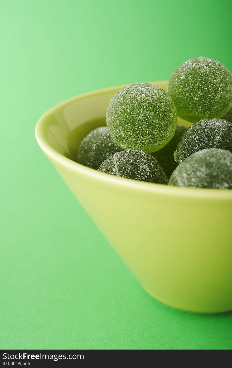 Green marmalade balls in the bowl on the green background