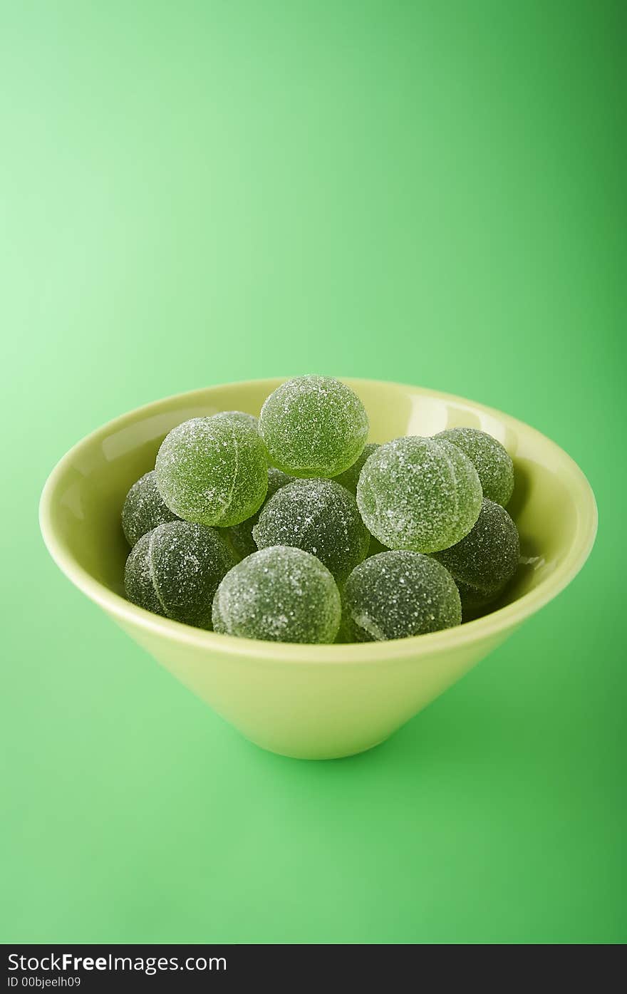 Green marmalade balls in the bowl on the green background