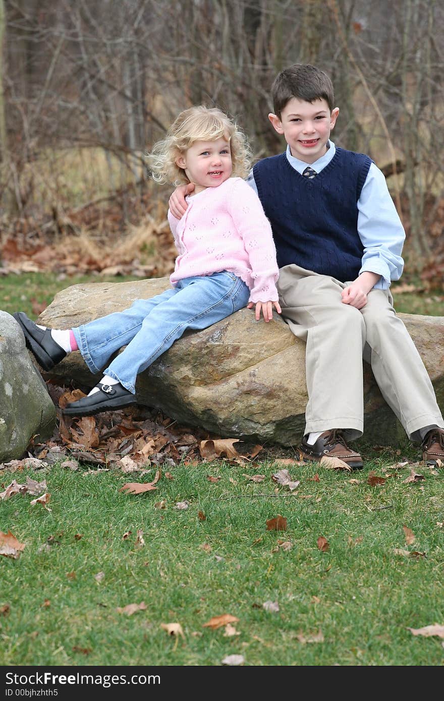 Happy young children siblings in park like setting on rocks. Happy young children siblings in park like setting on rocks.