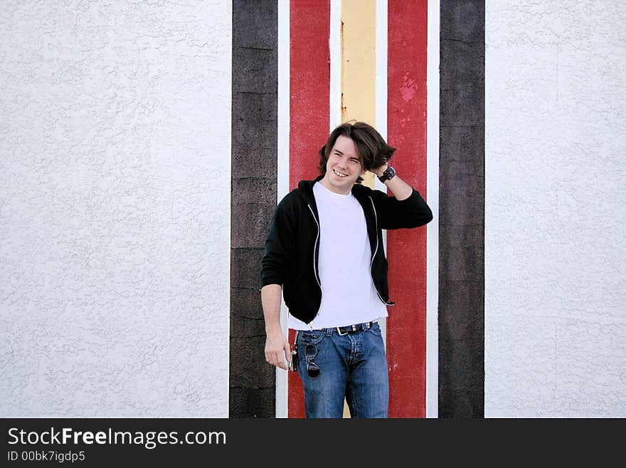 Photo of a young man standing outside in front of a striped wall. Photo of a young man standing outside in front of a striped wall