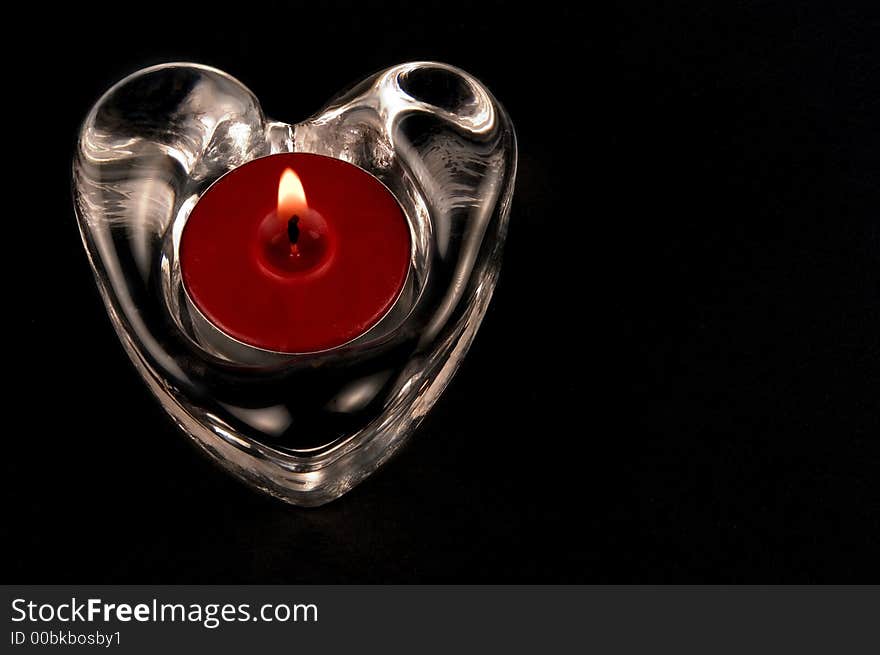 Valentines heart in glass  with candle isolated one a black background. Valentines heart in glass  with candle isolated one a black background