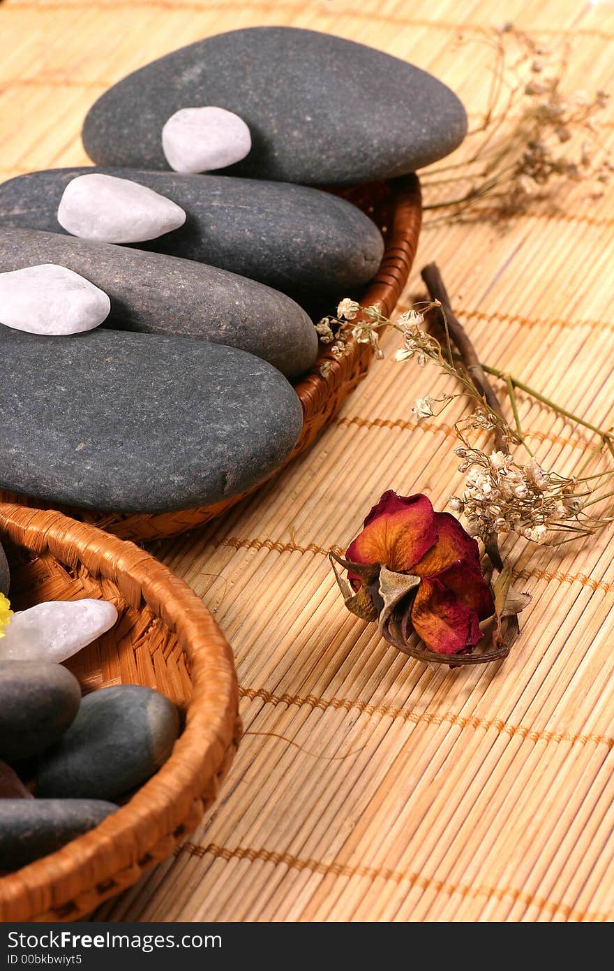 Natural pebbles and dried rose petals on the rattan background. Suitable for spa and relaxation setting. Natural pebbles and dried rose petals on the rattan background. Suitable for spa and relaxation setting.