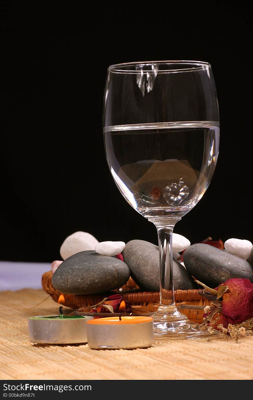 A romance view of a glass, natural pebbles and dried rose petals on the rattan background. Suitable for spa, relaxation and romance setting. A romance view of a glass, natural pebbles and dried rose petals on the rattan background. Suitable for spa, relaxation and romance setting.