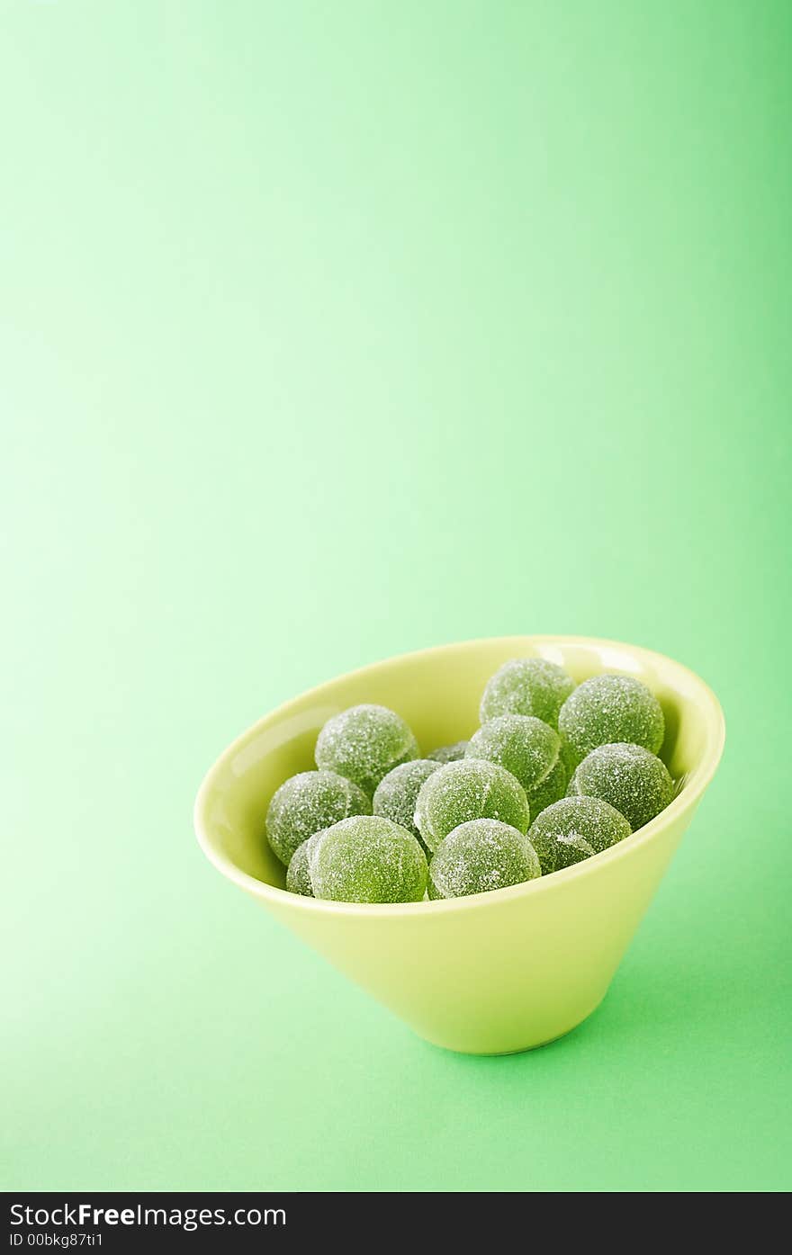 Green marmalade balls in the bowl on the green background