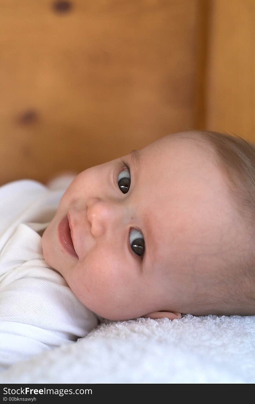 Image of baby boy wearing a white onesie lying on a bed. Image of baby boy wearing a white onesie lying on a bed