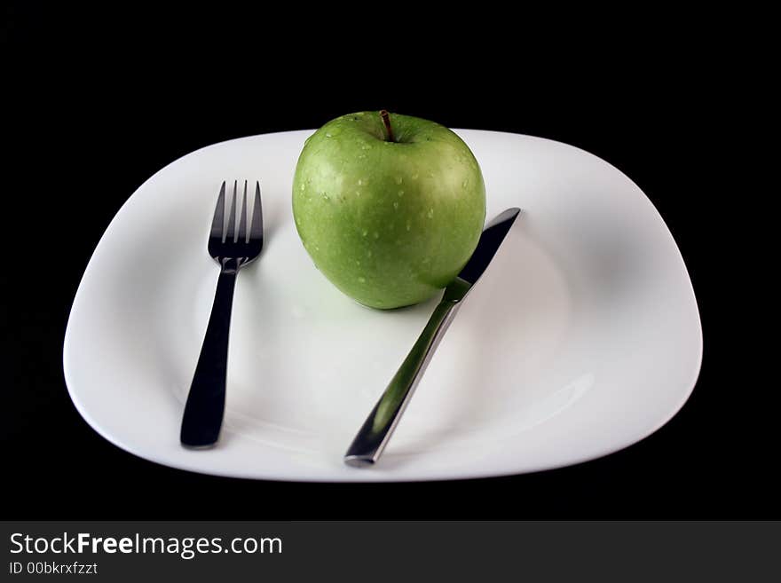 Green apple on a plate with fork and knife