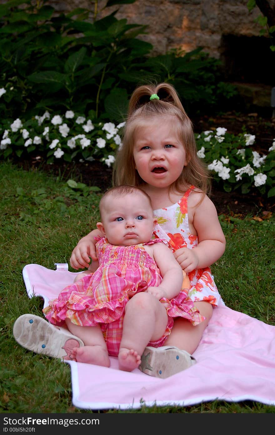 Two very young girls sitting on a blanket in a park making very grumpy faces. Two very young girls sitting on a blanket in a park making very grumpy faces.