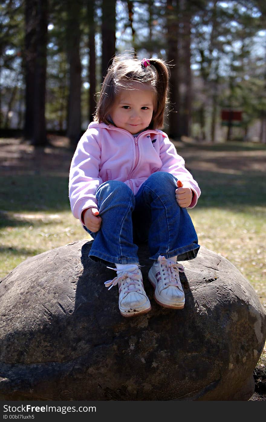 Four year old girl sitting on a rock in a park. Four year old girl sitting on a rock in a park.