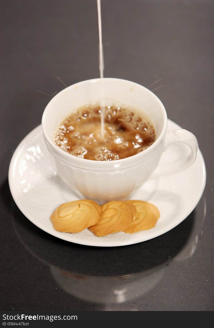 Pouring milk into coffee and cookies isolated on black