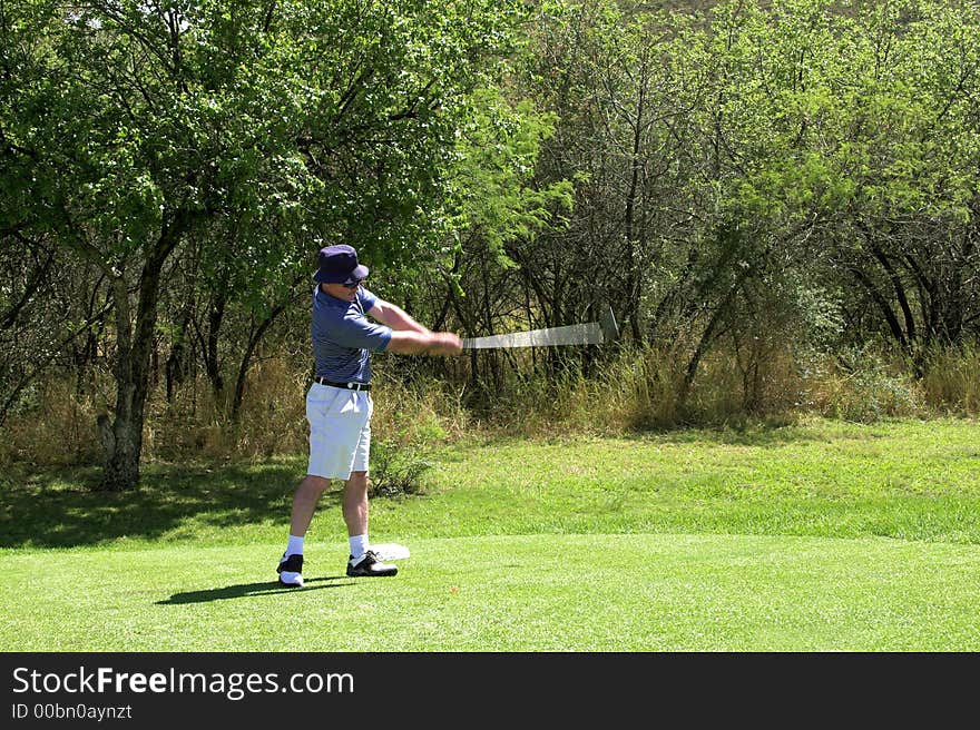 Golfer in striped shirt hitting the ball from the tee box. Golf club and arms of the golfer are in motion. . Golfer in striped shirt hitting the ball from the tee box. Golf club and arms of the golfer are in motion.