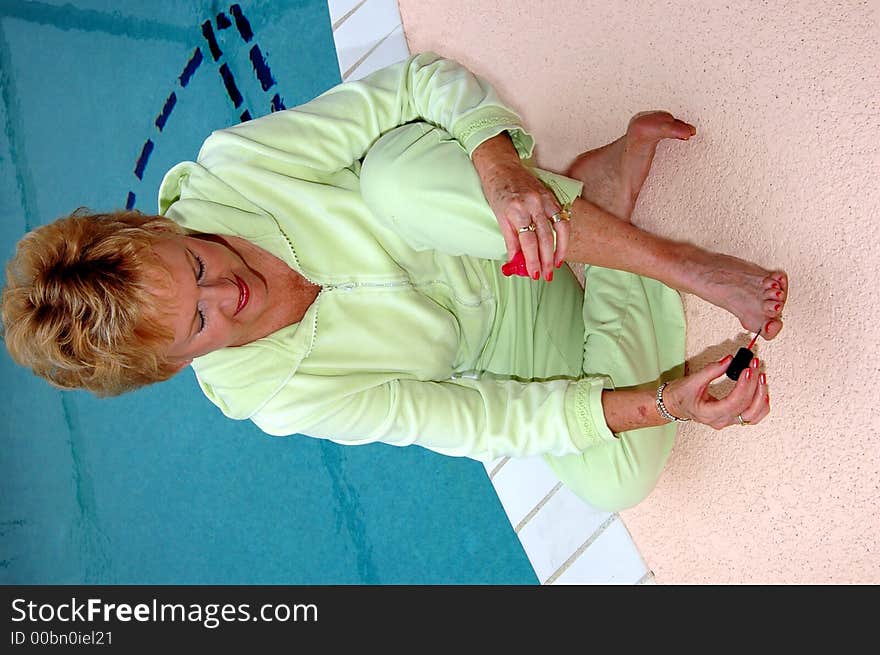 A senior woman painting her toe nails by the pool. A senior woman painting her toe nails by the pool