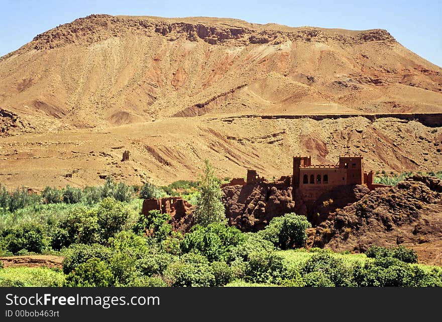 Typical valley in southern Morocco with some green trees and meadows, bare red hills, small clay castle. Typical valley in southern Morocco with some green trees and meadows, bare red hills, small clay castle.