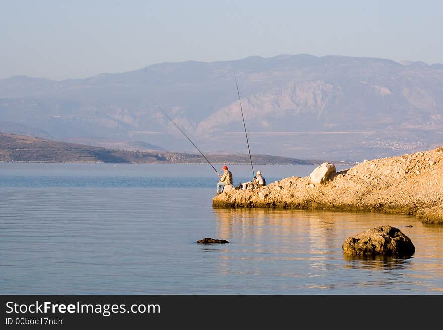 Two fishermen catch fish seafishing in greece  rock coast. Two fishermen catch fish seafishing in greece  rock coast