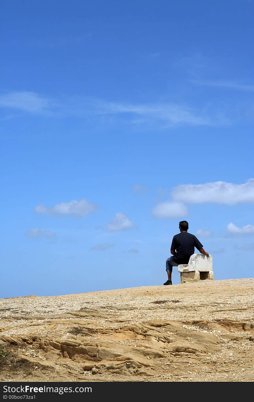 Man sitting on a bench with blue cloudy sky