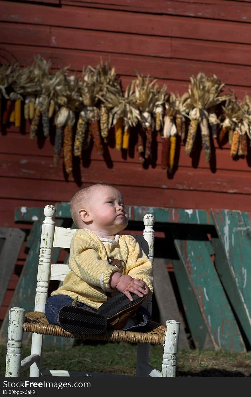 Image of baby boy sitting on a chair in front of a red farm building. Image of baby boy sitting on a chair in front of a red farm building