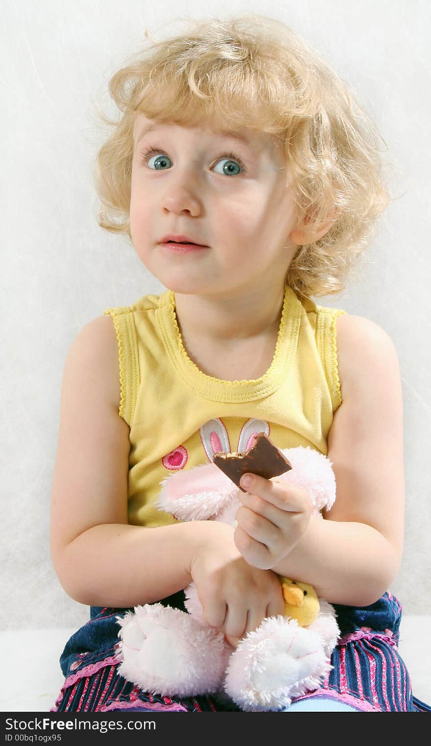 Little Blonde Curly Girl Eating Chocolate With Toy