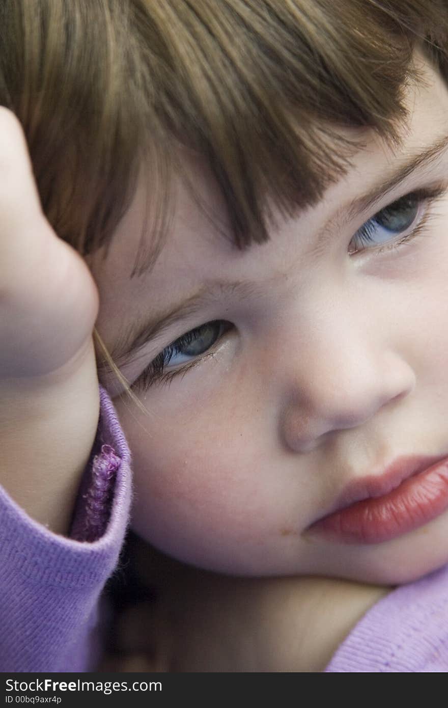 Cute little brunette girl holding her face while looking right of camera. Cute little brunette girl holding her face while looking right of camera