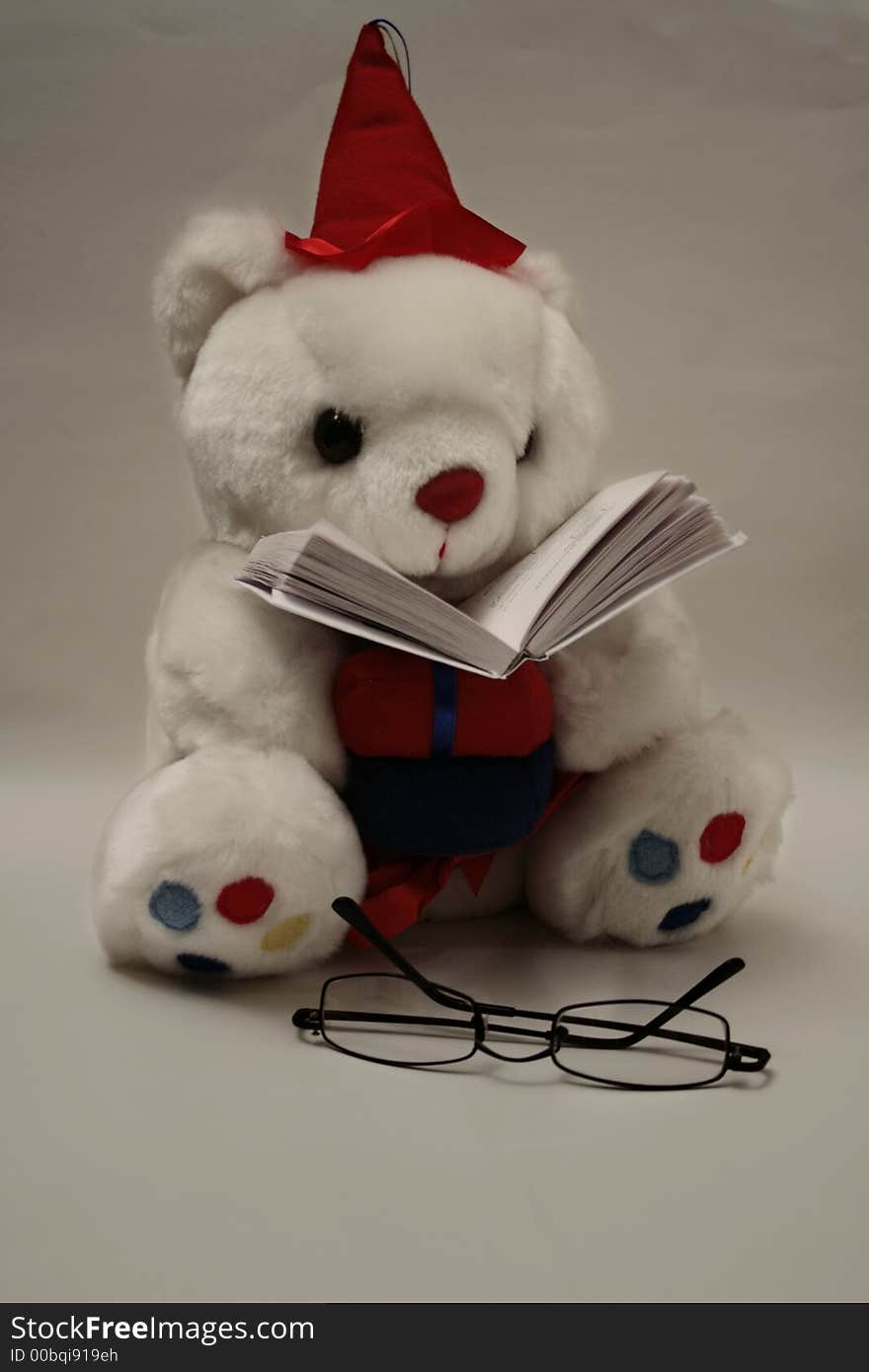 Sitting and reading teddy bear with glasses near and the book under its face