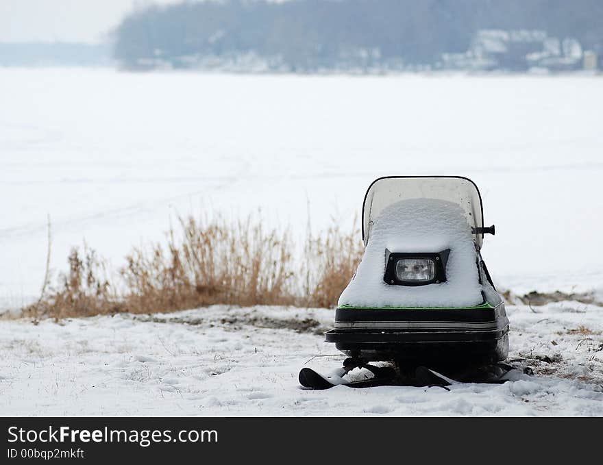 A snow covered child's snowmobile sitting side of frozen lake. A snow covered child's snowmobile sitting side of frozen lake.