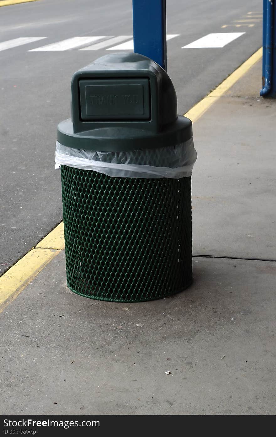 A Green Trash can on the side of a pavement