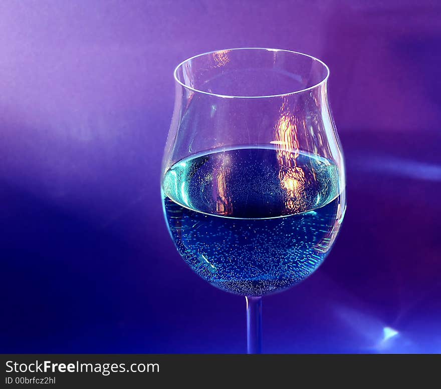 One glass with a drink and a reflection of a near fireplace on blue background. One glass with a drink and a reflection of a near fireplace on blue background