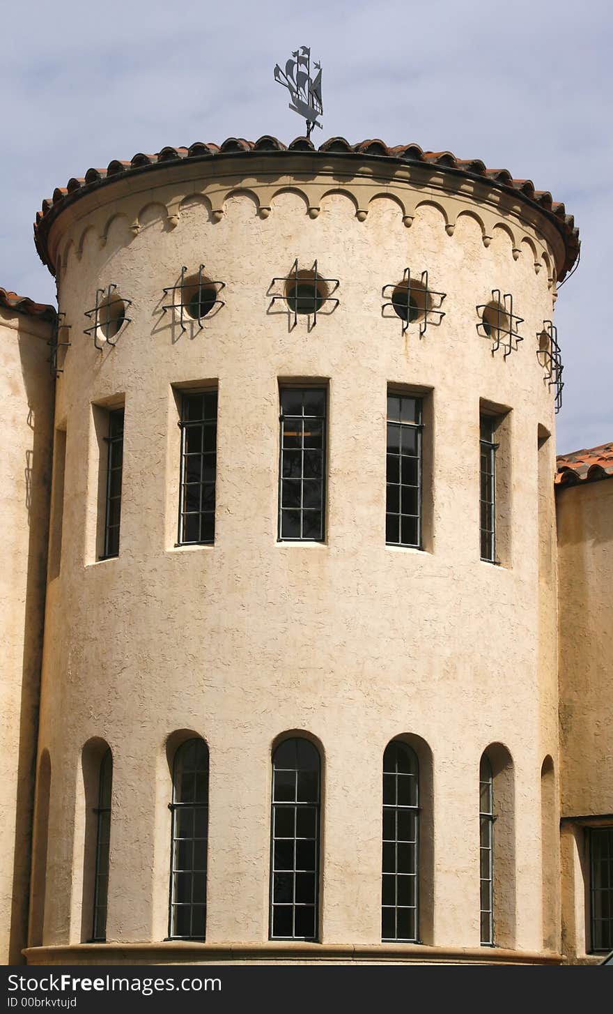 Round portion of Mediterrarean building with weathervane and unusual windows: round, tall rectangular and tall arched. Round portion of Mediterrarean building with weathervane and unusual windows: round, tall rectangular and tall arched