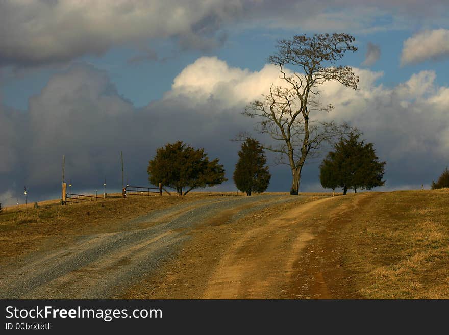 Country lane goes across hilltop in winter against dramatic sky and trees like a painting. Country lane goes across hilltop in winter against dramatic sky and trees like a painting