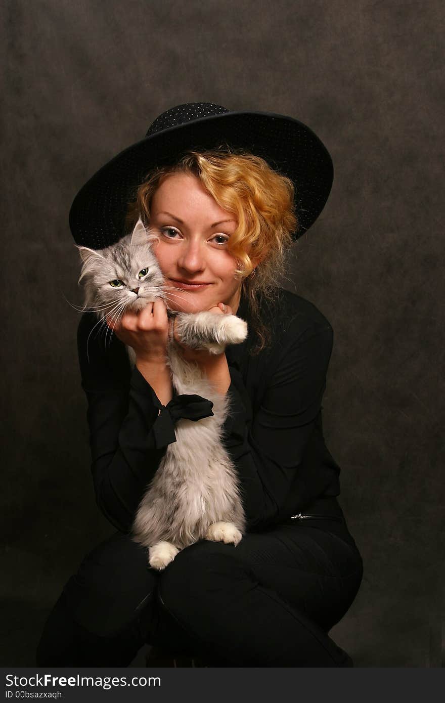 The beautiful girl in a black hat covers a kitten. The beautiful girl in a black hat covers a kitten